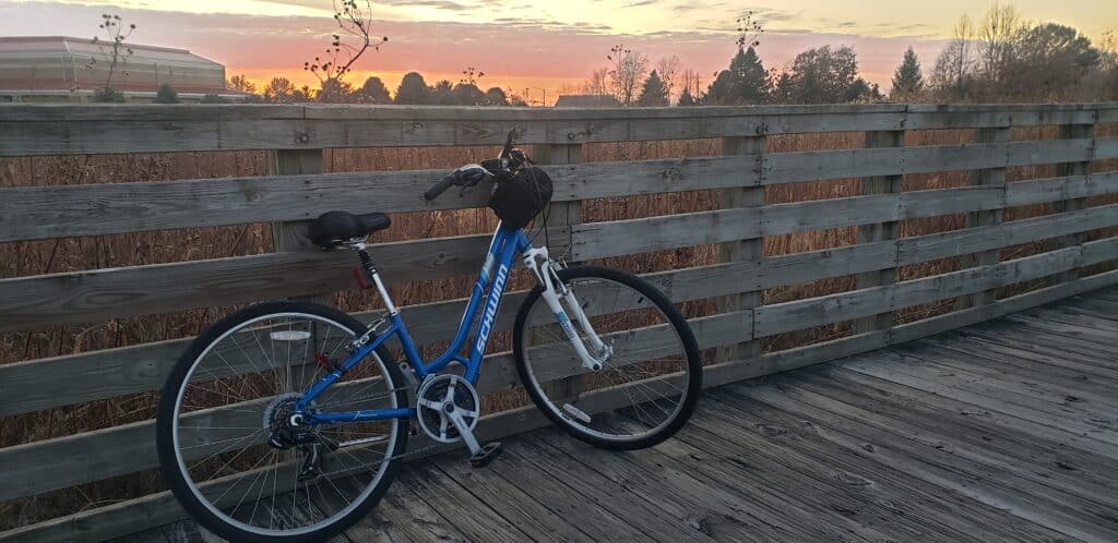 Blue bicycle resting against a wooden trail railing at sunset during a bike ride.